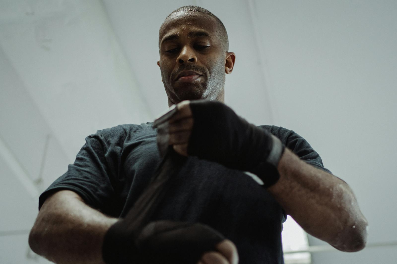 A focused athlete prepares for training by wrapping his hands with black gloves in a gym.