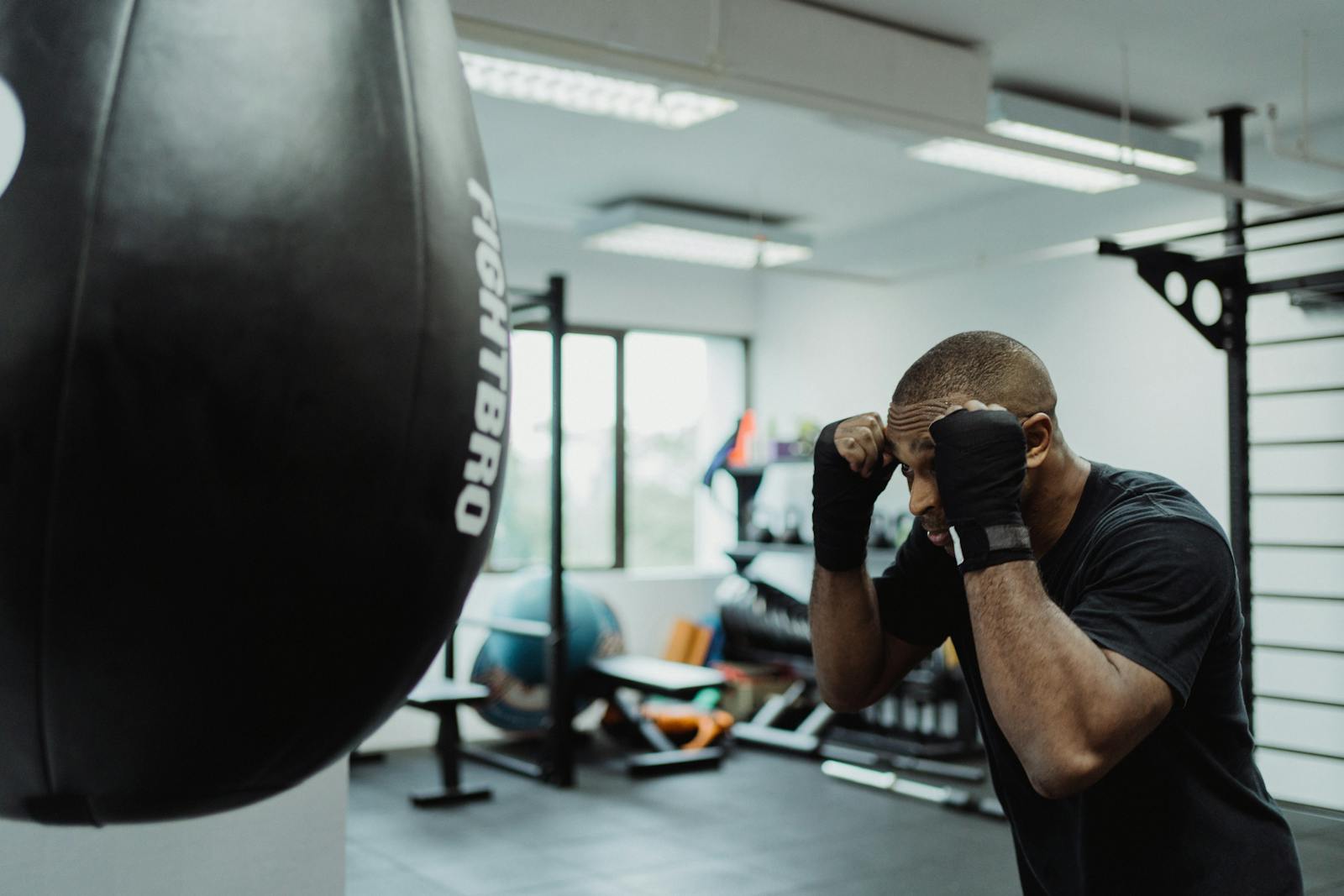 Determined boxer training with a punching bag inside a gym, showcasing focus and strength.